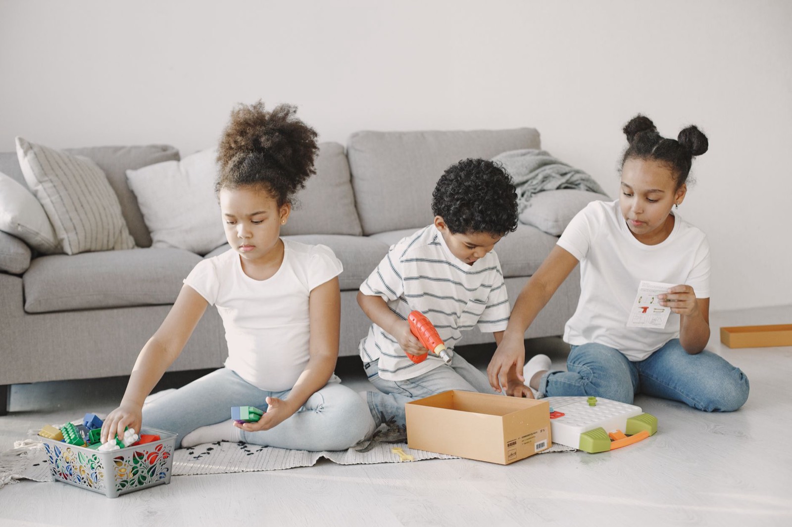 Deux enfants jouent dans un salon pendant que la jeune fille au pair les surveille
